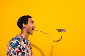 Side profile photo of young man wearing stylish t shirt open mouth magician spitting dollar banknotes isolated on yellow color background