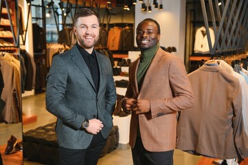 Two stylish multiracial men standing in classic suits standing in a clothing store
