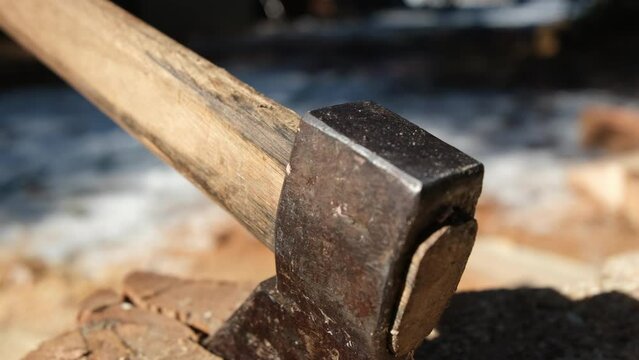 Extreme close up of home made Russian style ax impaled in chunk of wood and mowing camera away exposing whole oak logs ready to be split into firewood.