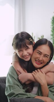 Vertical clip. Mother and daughter hugging each other happily. Young mother and little daughter are spending time together at home.	