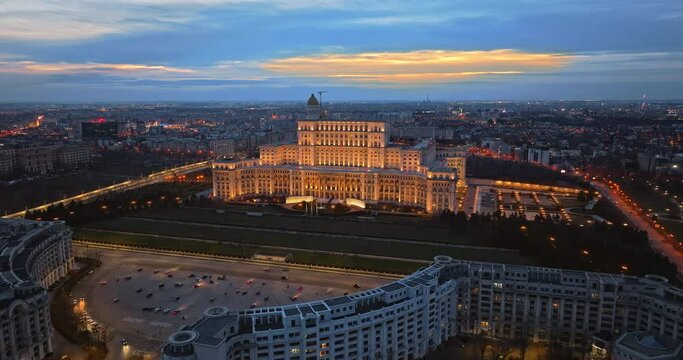 Aerial drone view of illuminated Palace of the Parliament in Bucharest downtown in the evening. Multiple districts around. Romania