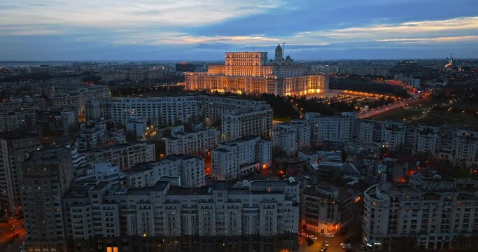 Aerial drone view of illuminated Palace of the Parliament in Bucharest downtown in the evening. Multiple districts around. Romania