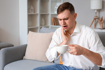 Fototapeta na wymiar Young man with cup of tea suffering from toothache at home