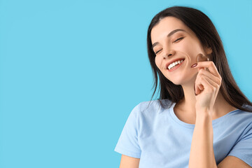 Young woman with heart-shaped chocolate candy on blue background, closeup