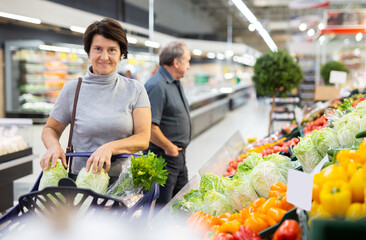 Mature female customer selects savoy cabbage with interest in grocery department of supermarket