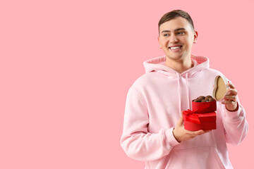 Young man with box of heart-shaped chocolate candies on pink background