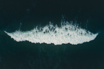 Aerial view of a symmetrical wave and the surfer swimming in Portugal.