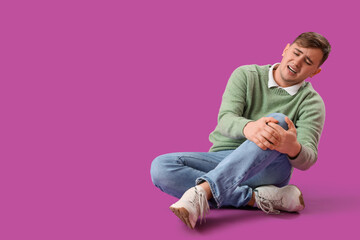 Young man suffering from knee pain on purple background