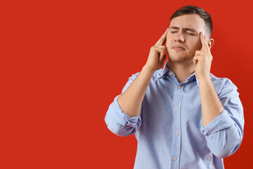 Young man suffering from headache on red background