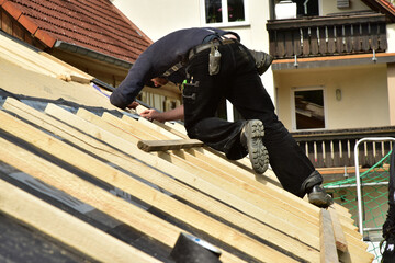 Dachdecker beim Verlegen und befestigen der Dachlatten eines Steildachs auf der Holzfaserdämmung für die Eindeckung mit Ziegeln - obrazy, fototapety, plakaty