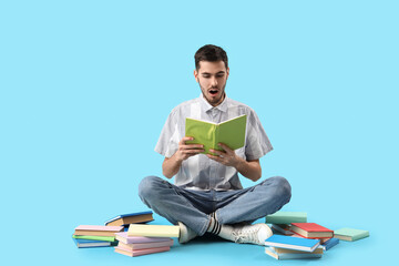 Shocked young man reading book on blue background