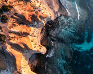 Aerial view of limestone cliffs with a warm sunset hue and blue coastal water from above, Port Willunga, South Australia, Australia.