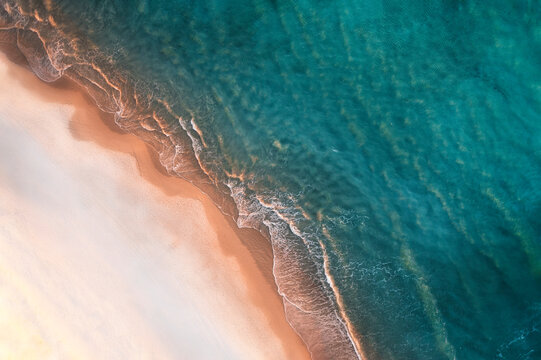 Aerial view of a sandy beach from above with turquoise blue water and calm waves rolling onto shore, Port Noarlunga, South Australia, Australia.