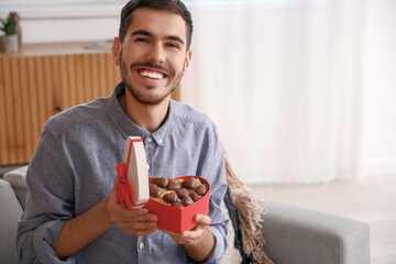 Young man with box of heart-shaped chocolate candies at home