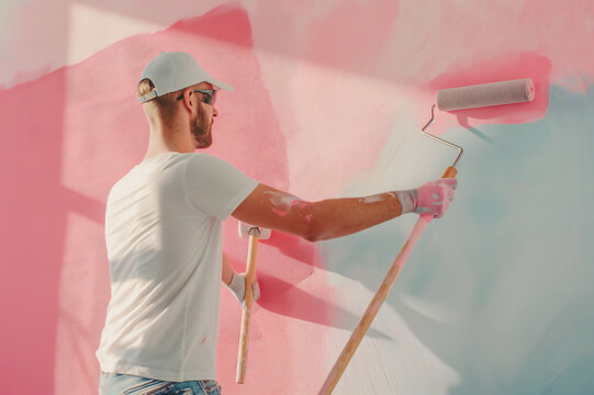 A male painter applies pastel paints to a wall with a roller, a blank space on a colorful wall