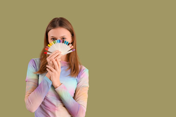 Young woman with nail polishes palette on green background