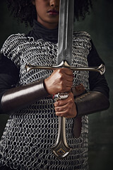 Close-up of African woman in chainmail holding sword vertically in front of face against vintage...