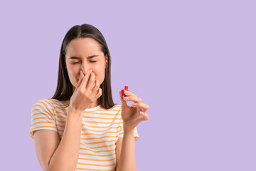 Displeased young woman with nail polish covering her nose on lilac background