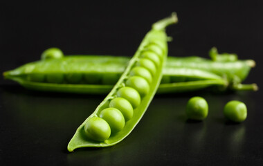Closed and open pod of green peas with large grains on a black background, close-up.