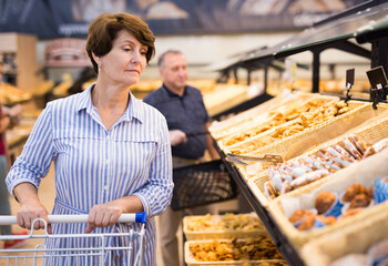Elderly retired senora buying bread and pastries in grocery section of the supermarket