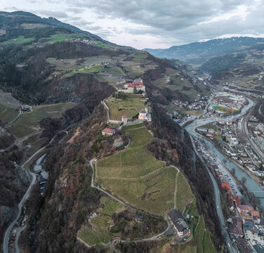 Aerial view of Sabiona Monastery and Chiusa town with winding roads and terraced vineyards, Klausen, South Tyrol, Italy.
