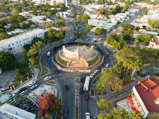 Aerial view of Paseo de Montejo, Monumento a la Bandera roundabout with traffic, trees, and shadows in evening, Merida, Yucatan, Mexico.