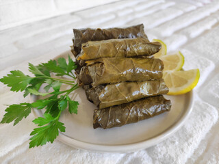 Delicious traditional oriental dolma made of grape leaves stuffed with rice on a plate with parsley and lemon slices