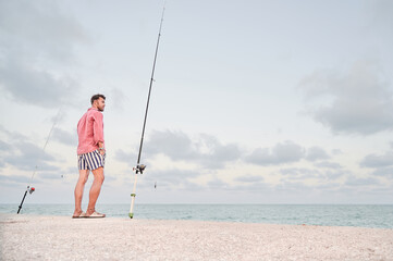 Adult man with two fishing rods in front of the sea looks at the horizon on the breakwater while...