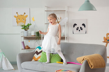 Cute little girl dressed as fairy on sofa at home