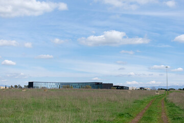 Fototapeta na wymiar Horizontal landscape - under the blue sky on the horizon the mirrored long modern building, seen across a field with green grass