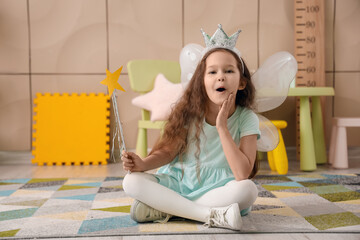 Surprised little girl dressed as fairy sitting in bedroom