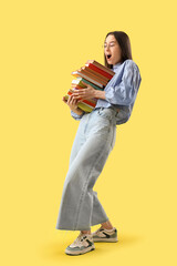 Shocked young woman with stack of books on yellow background