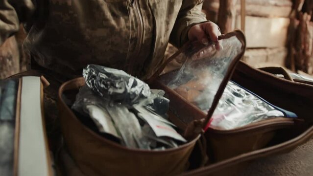 A female military medic attentively organizes her medical supplies in a weathered kit bag, preparing for emergency response in a rugged environment. Camera 8K RAW. 