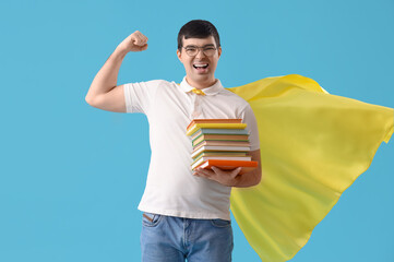 Young man in superhero cape with books showing muscles on blue background