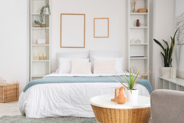 Interior of light bedroom with big bed, shelf units and frames