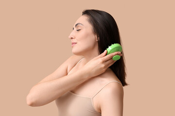 Beautiful young woman using hair scalp massager on brown background - obrazy, fototapety, plakaty