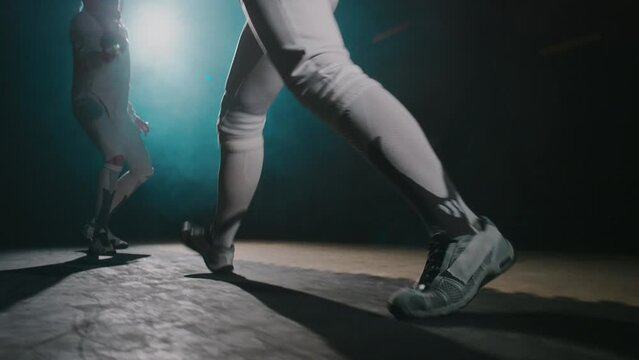 Ground level handheld footage of footwork of professional anonymous foil fencer fighting during duel in smoky room