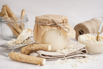 Jar of horseradish sauce with horseradish roots on white background