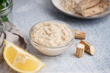 Horseradish sauce in glass bowl with lemon and horseradish roots on white background