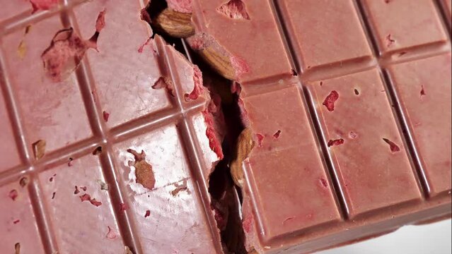 A breaking bar of pink ruby chocolate with freeze-dried strawberries and almonds close-up, . A healthy dessert based on berries and nuts