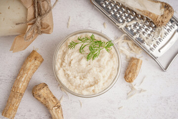 Fototapeta na wymiar Bowl of horseradish sauce with horseradish roots on white background. Top view