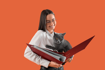 Young businesswoman with folder and cute British Shorthair cat on orange background