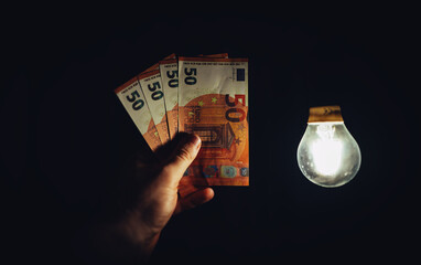 Man holds money next to a light bulb. Expensive electricity concept. - 763285405