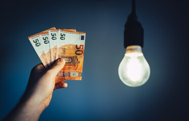 Man holds money next to a light bulb. Expensive electricity concept. - 763285407