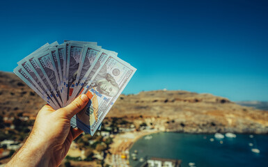 Man holds money against the backdrop of a beach in a warm country. - 763285425