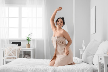 Happy young woman wearing towel after shower in bedroom