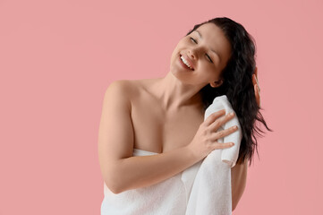 Young woman with towel wiping wet hair on pink background