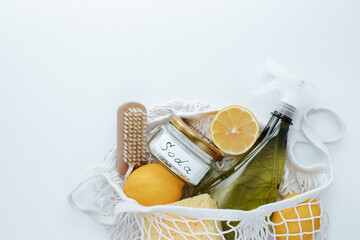 string bag on a white background with lemons, a wooden brush, a green spray bottle, a washcloth and a can with the inscription "soda". without people