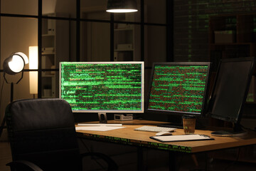 Computer monitors with programming code on table in dark office at night
