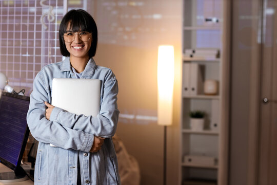 Happy female programmer with laptop in office at night